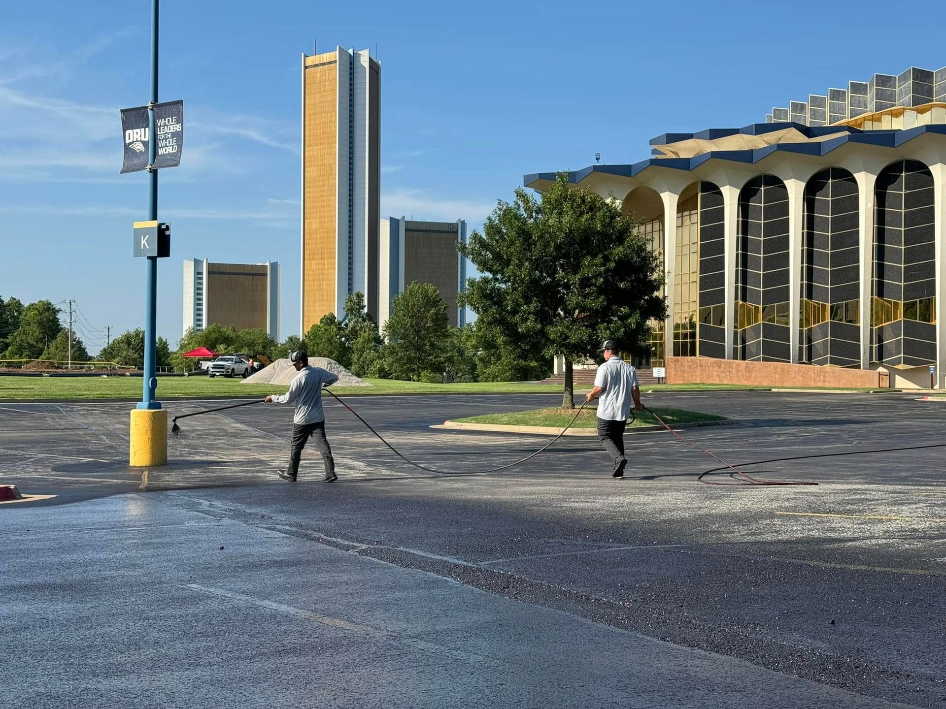 Two people crossing a wet plaza beside tall campus buildings on a sunny day