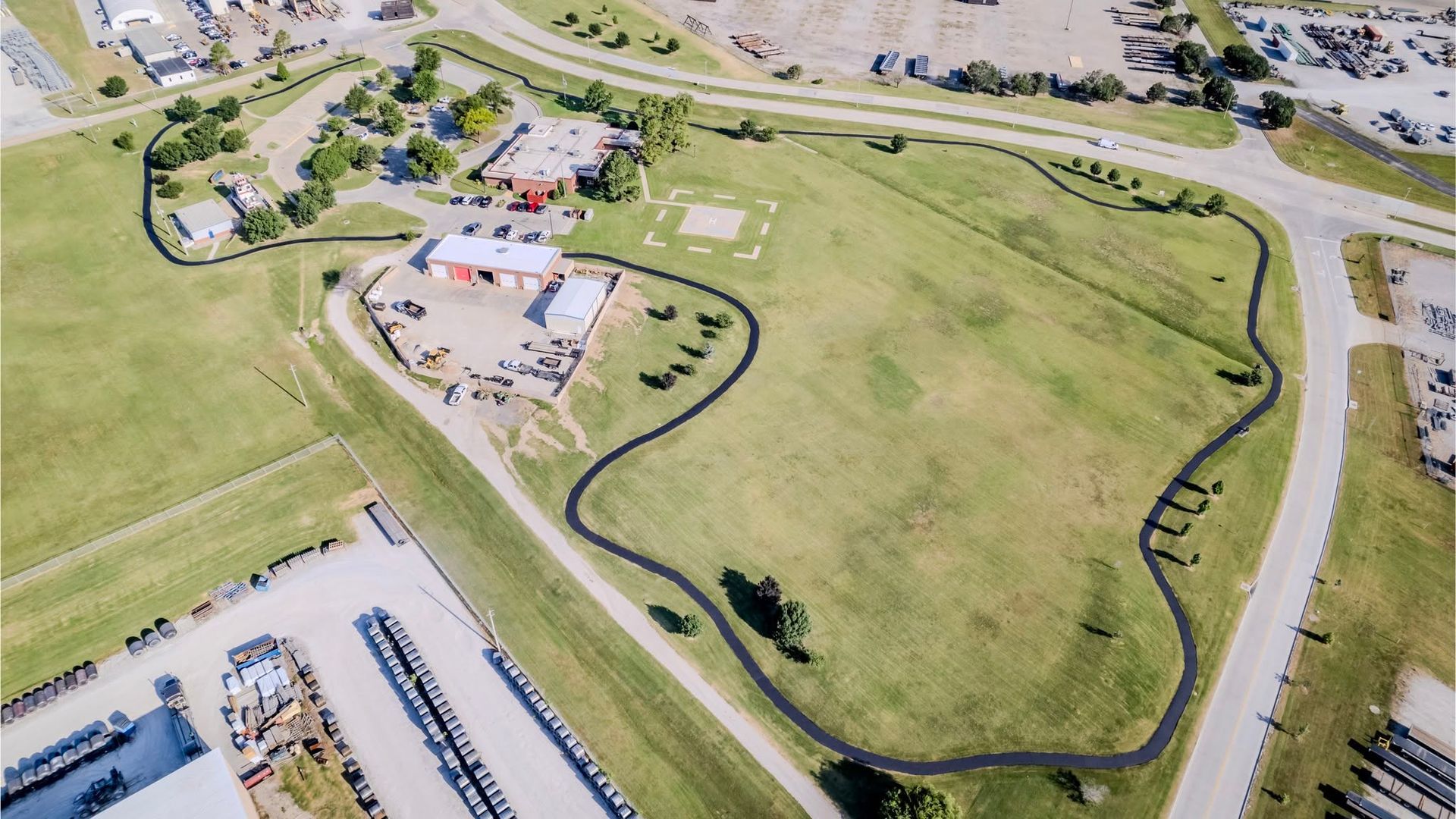 Aerial view of a grassy park with a small building, parking lots, and nearby roads.