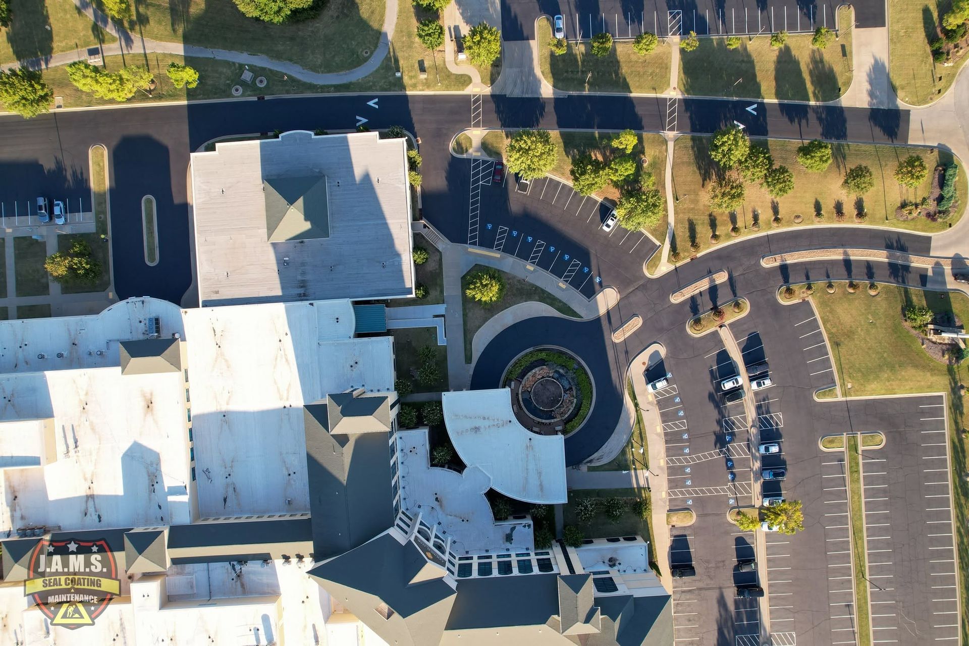Aerial view of a building complex with a circular driveway, parked cars, and surrounding trees and lots