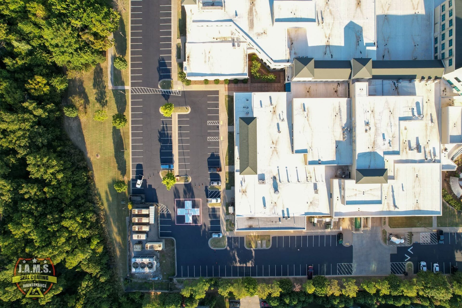 Aerial view of a building complex with a parking lot and surrounding trees