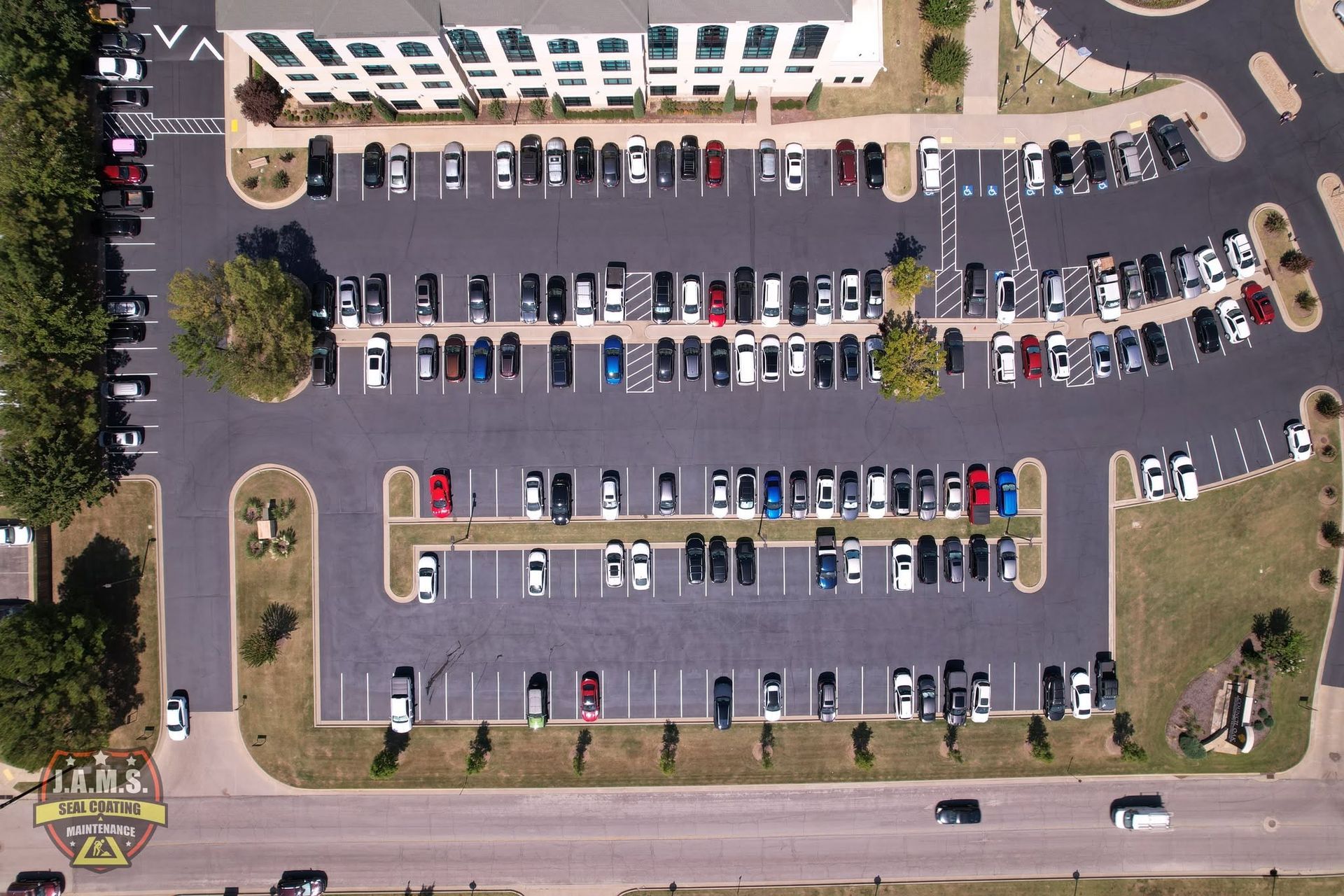 Aerial view of a parking lot with many parked cars beside a building and grassy edges.