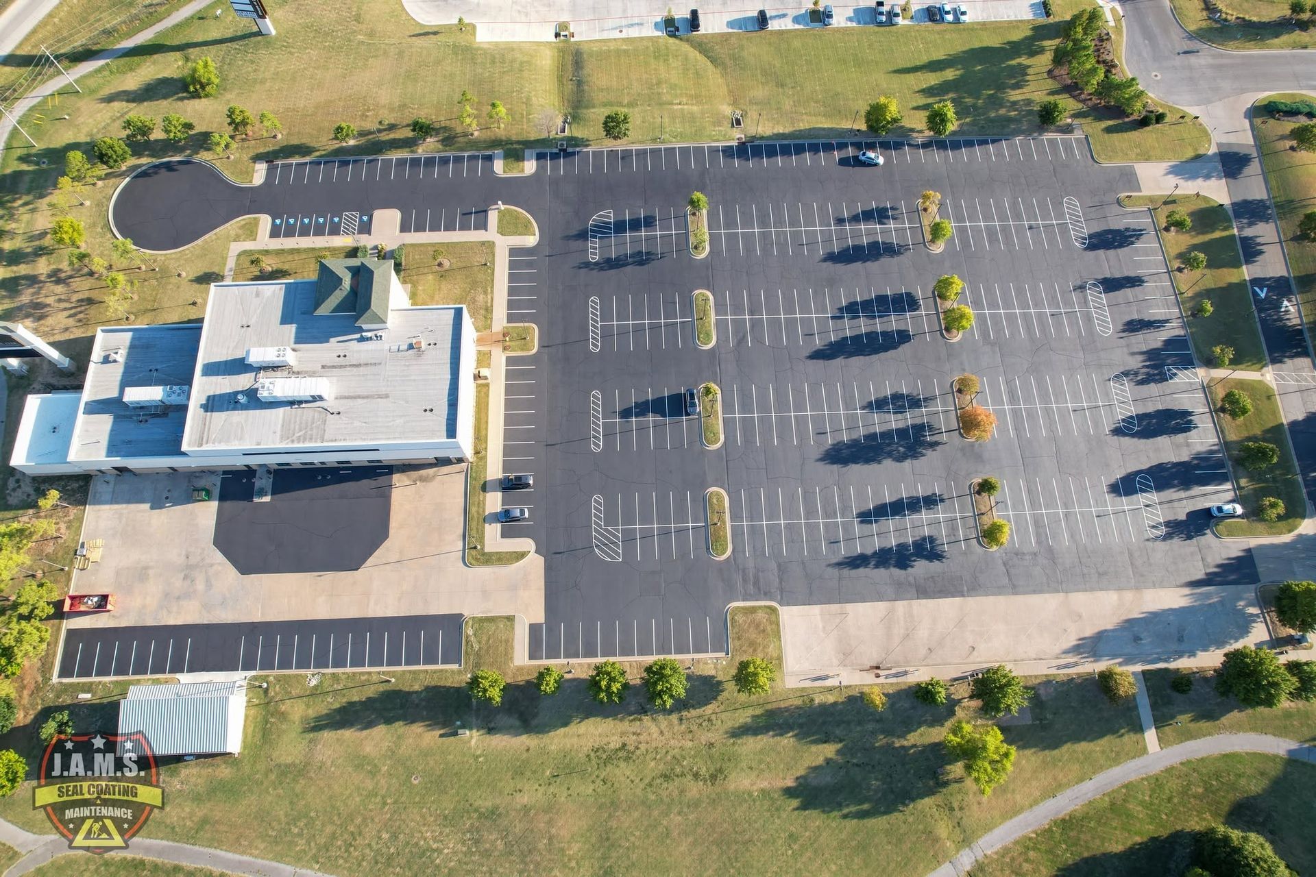 Aerial view of a building beside a large mostly empty parking lot with trees and walkways nearby