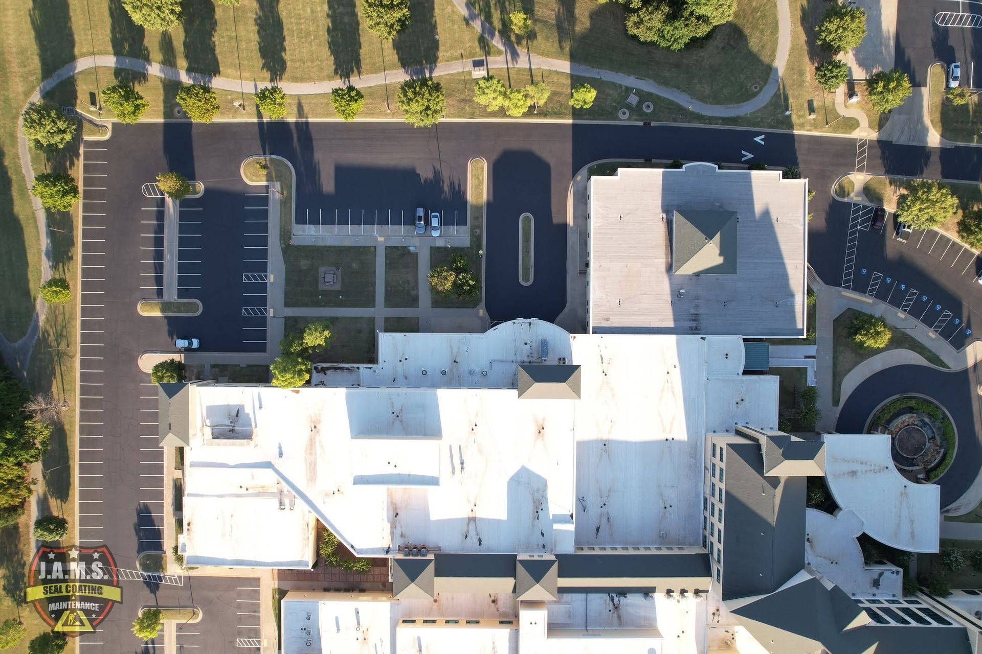 Aerial view of a large white building with parking lots, surrounded by roads and trees