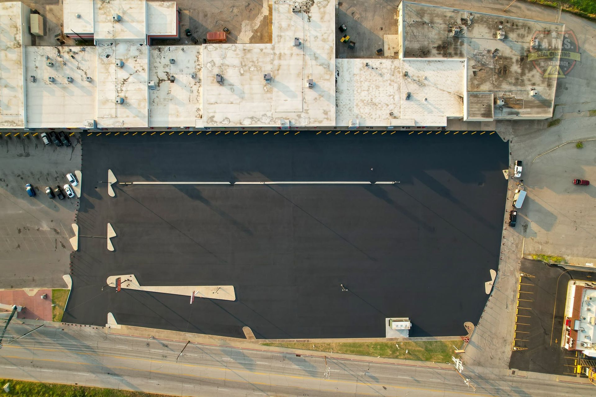 Aerial view of a dark asphalt lot beside a damaged building with debris and construction materials nearby