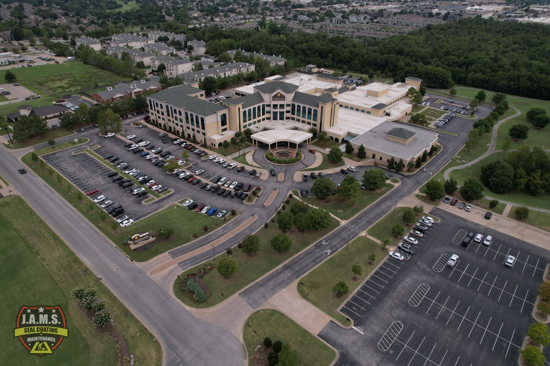 Aerial view of a large building with parking lots and surrounding trees on a hilltop
