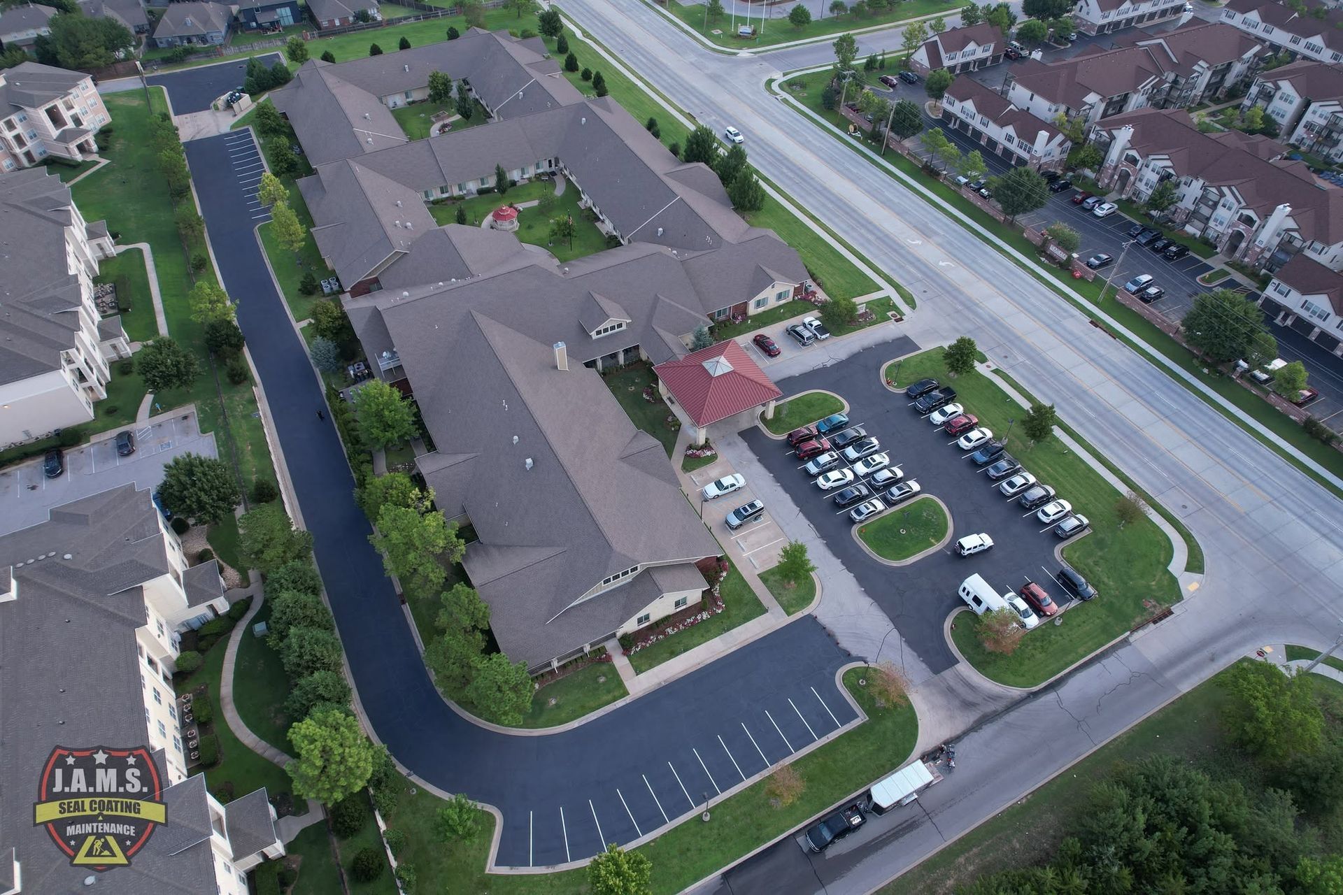 Aerial view of a large apartment complex with parking lots, roads, and surrounding homes.