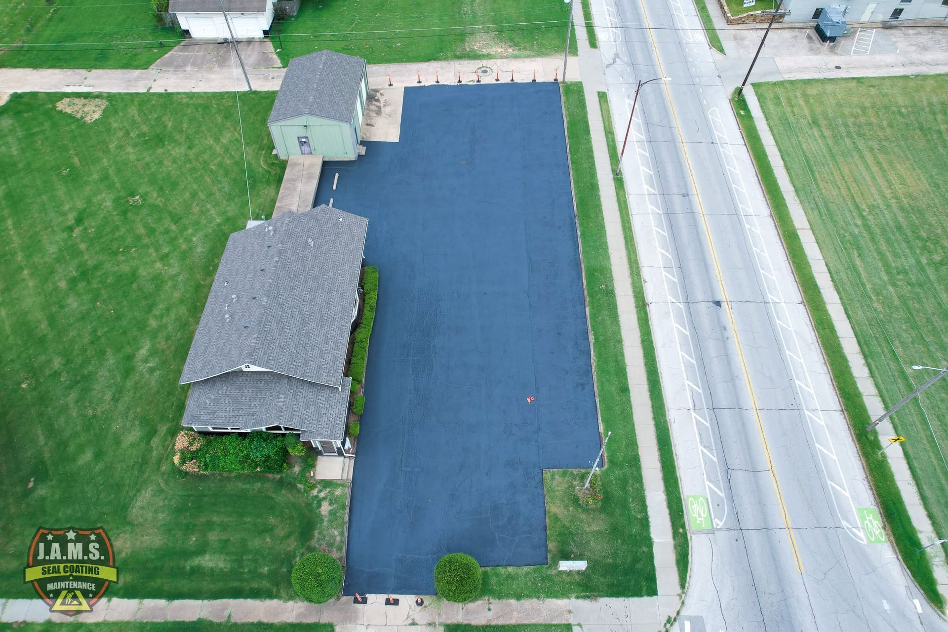 Aerial view of a house with a large dark-blue roof and green lawn beside a road