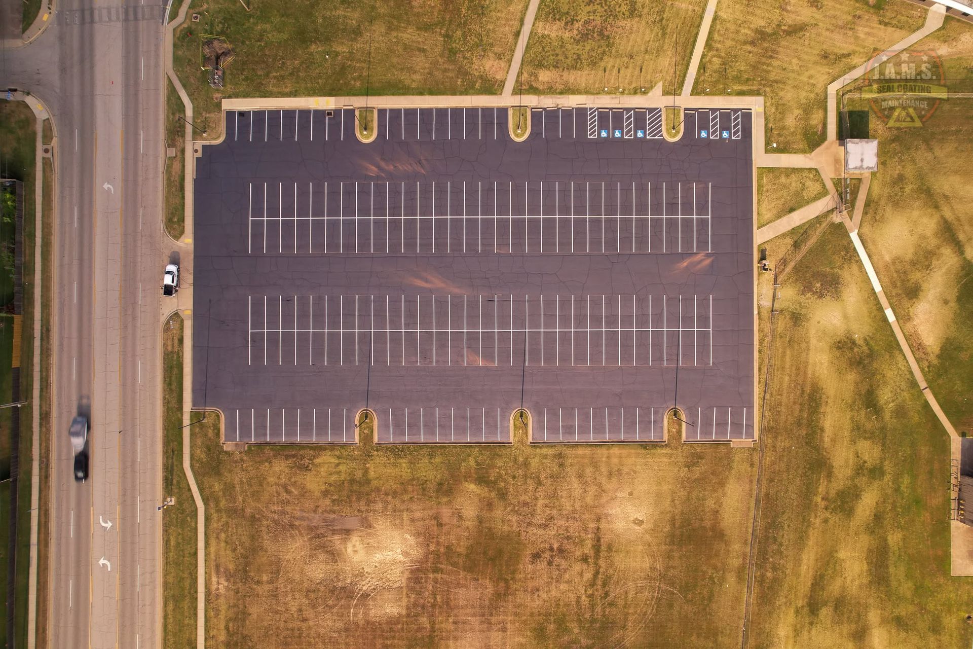 Aerial view of an empty parking lot beside a road and grassy field.