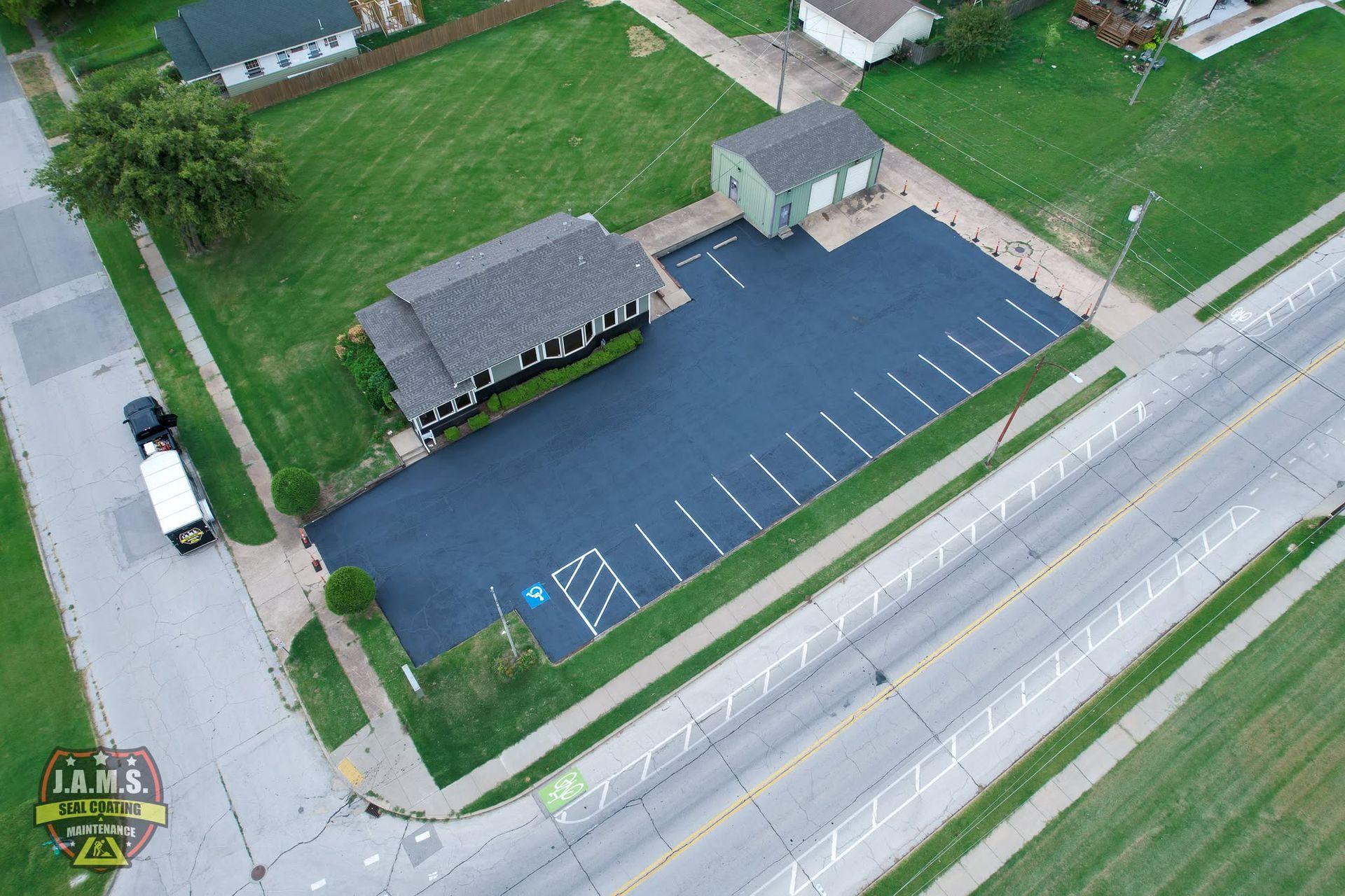 Aerial view of a small parking lot beside a building and road, with one white van and blue accessible spaces.