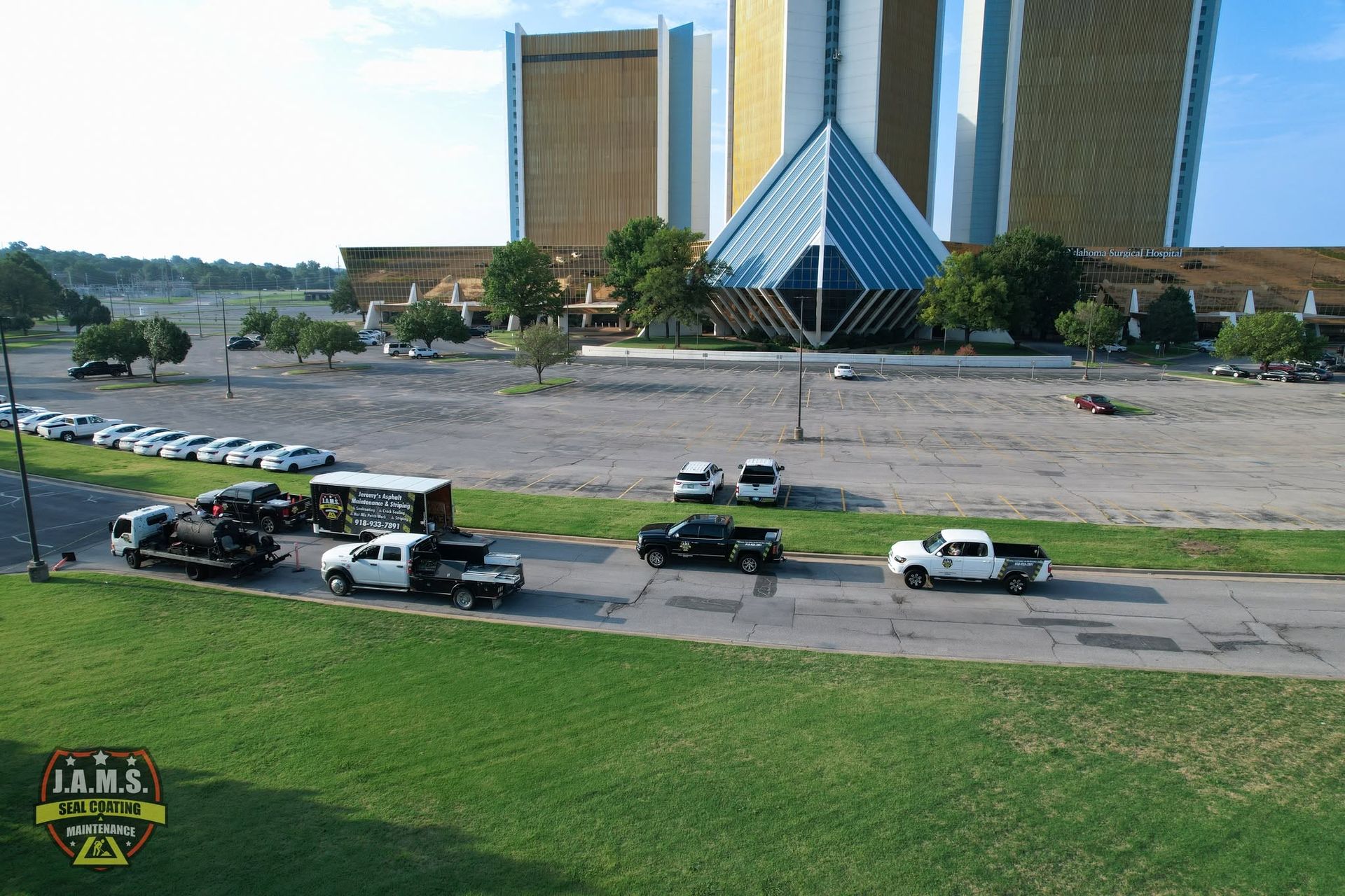 Trucks and cars parked on grass near a modern pyramid-topped building and tall towers.