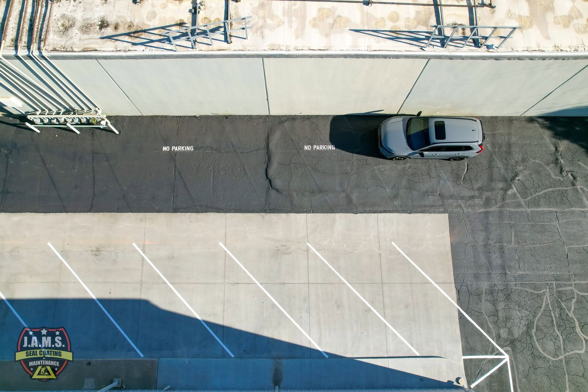 Overhead view of a gray car parked along an empty street beside a wall and parking lot markings