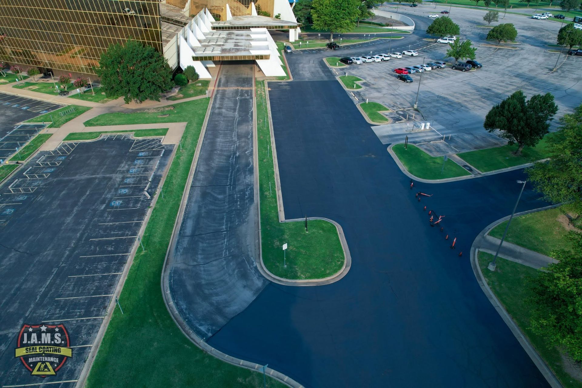 Aerial view of an empty parking lot with a building, trees, and wet pavement after rain.