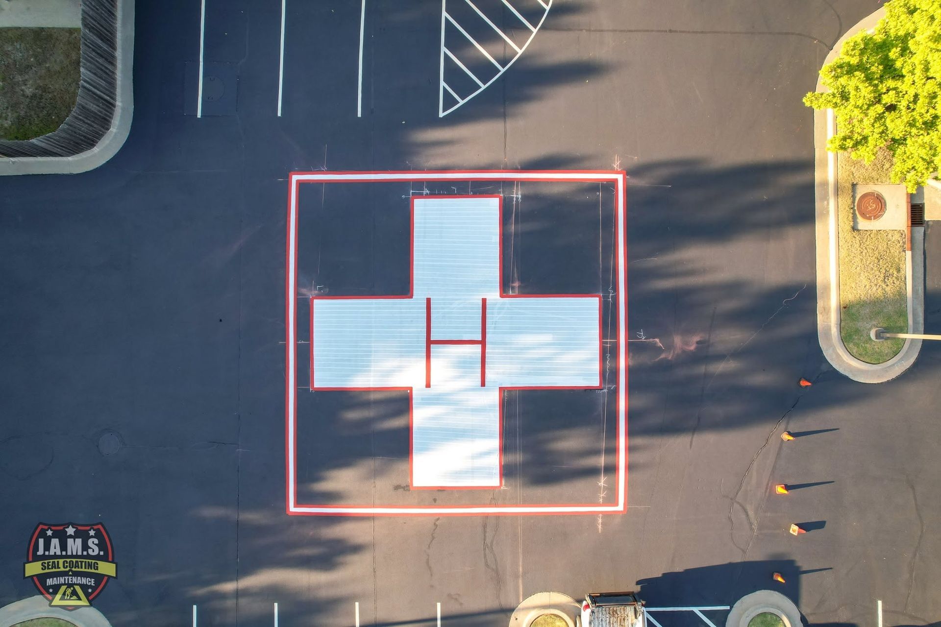 Aerial view of a white cross marker outlined in red painted on asphalt in a parking lot