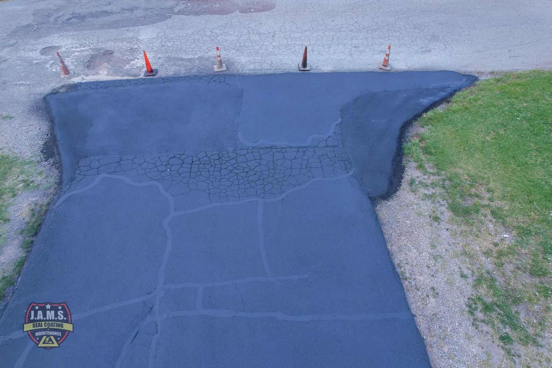 Freshly patched asphalt driveway with dark sealant and a grassy edge