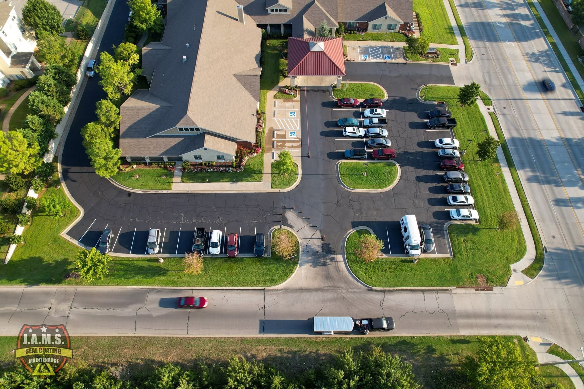 Aerial view of a parking lot beside a building, with several parked cars and a road along the bottom.