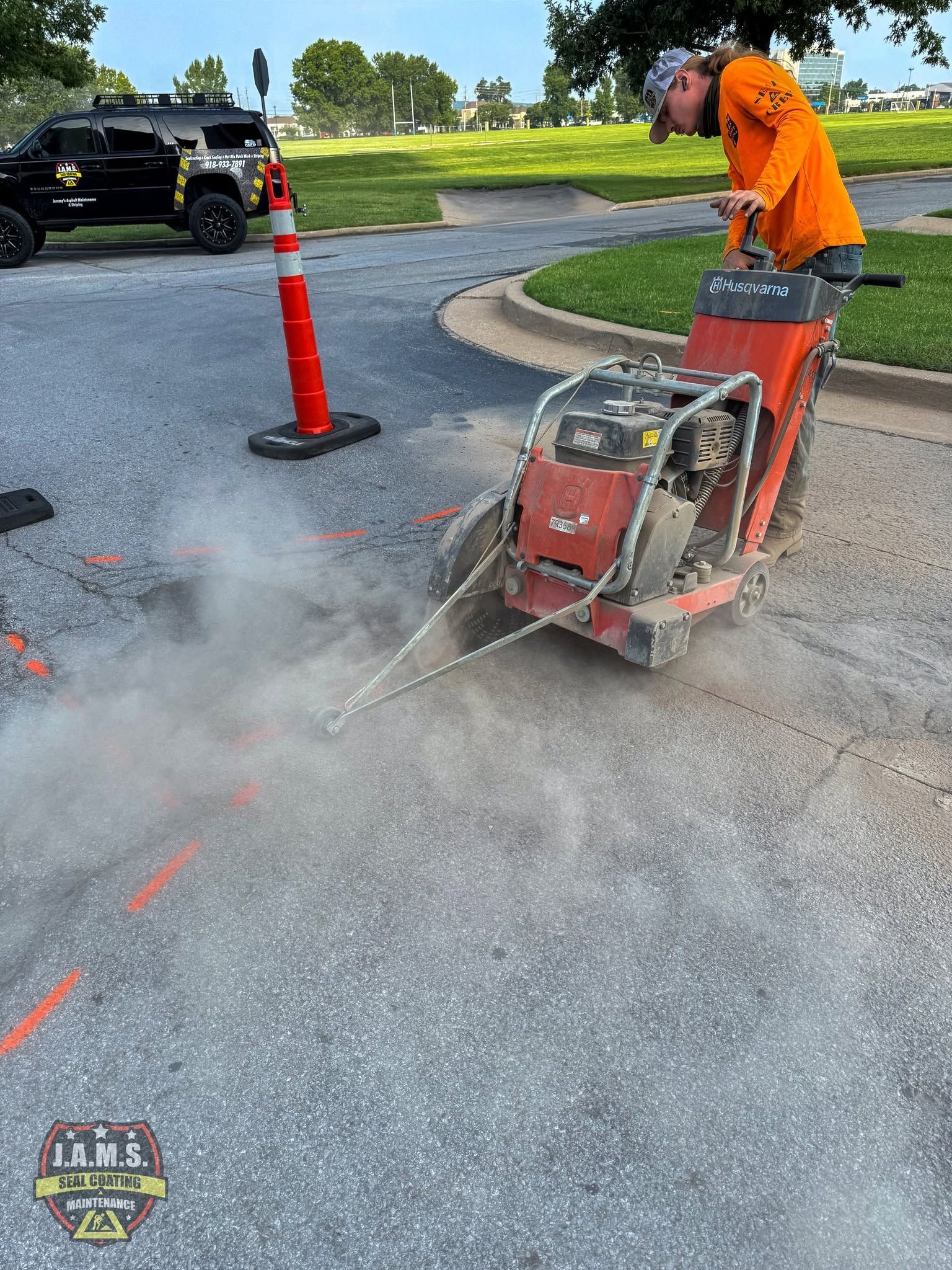 Worker power-washing asphalt beside traffic cones on a roadside.