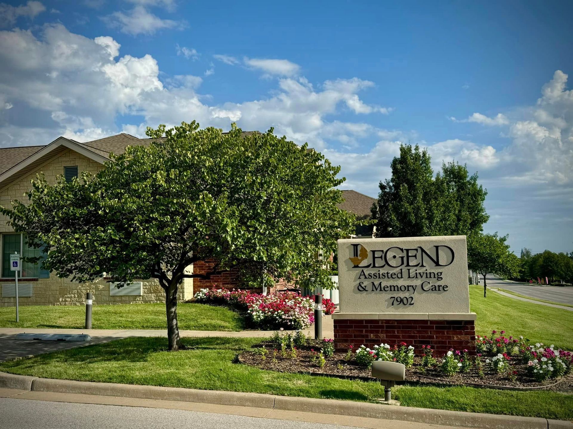 Stone sign for Legend Assisted Living Center in front of a landscaped building and trees under a blue sky.