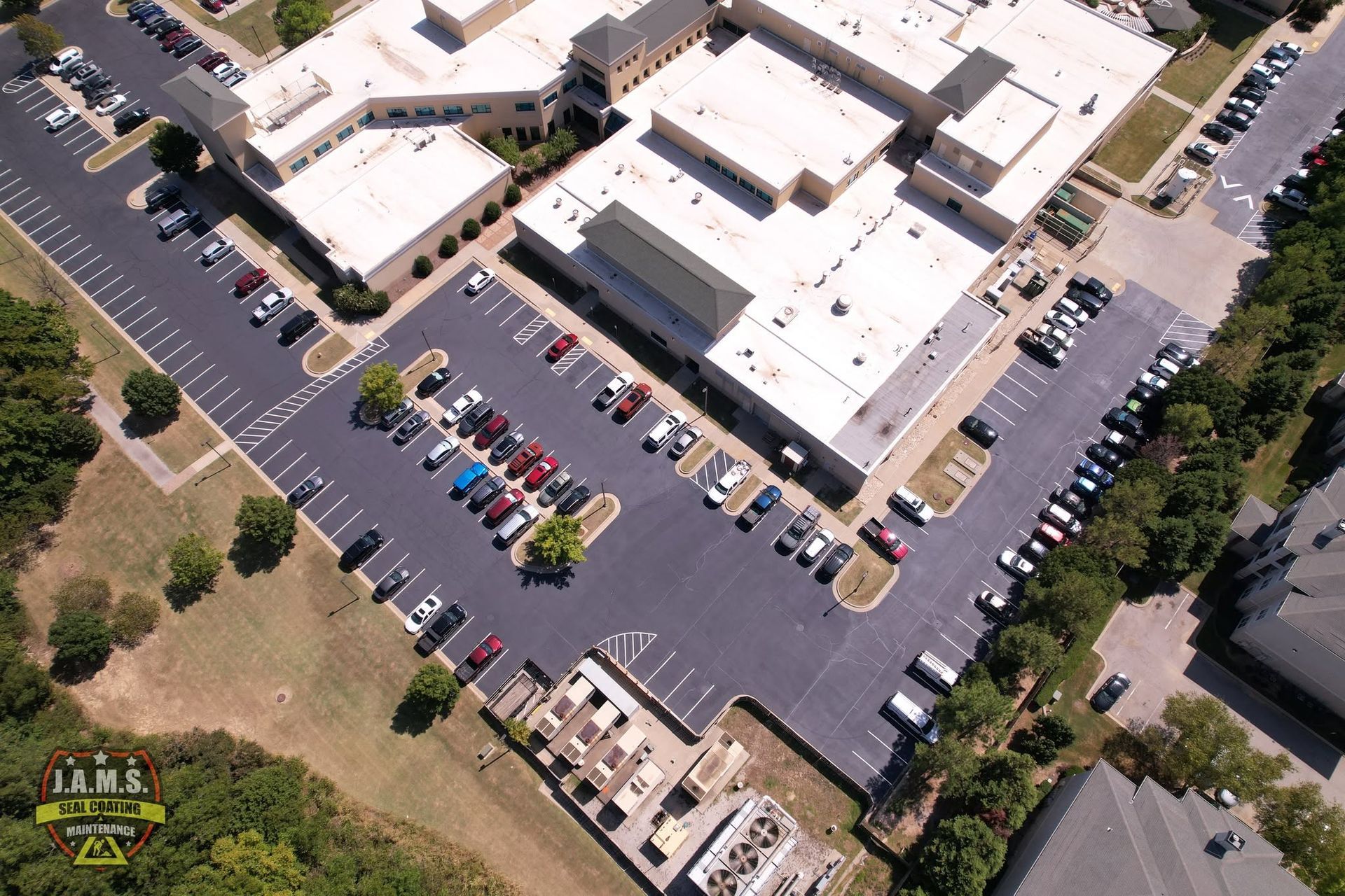 Aerial view of a school building with parking lots and many parked cars surrounded by trees.