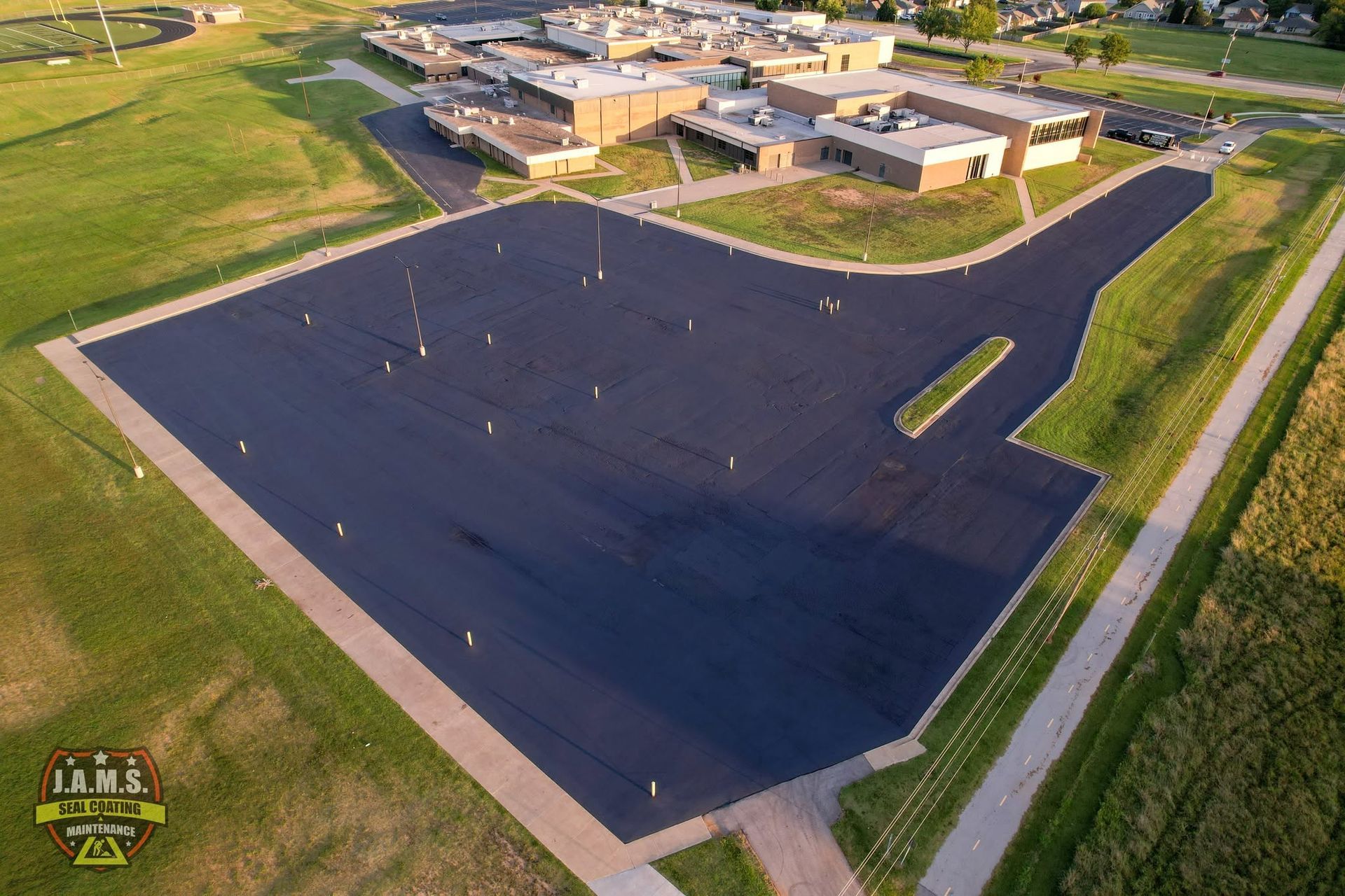 Aerial view of a freshly paved black lot beside a school building and green fields