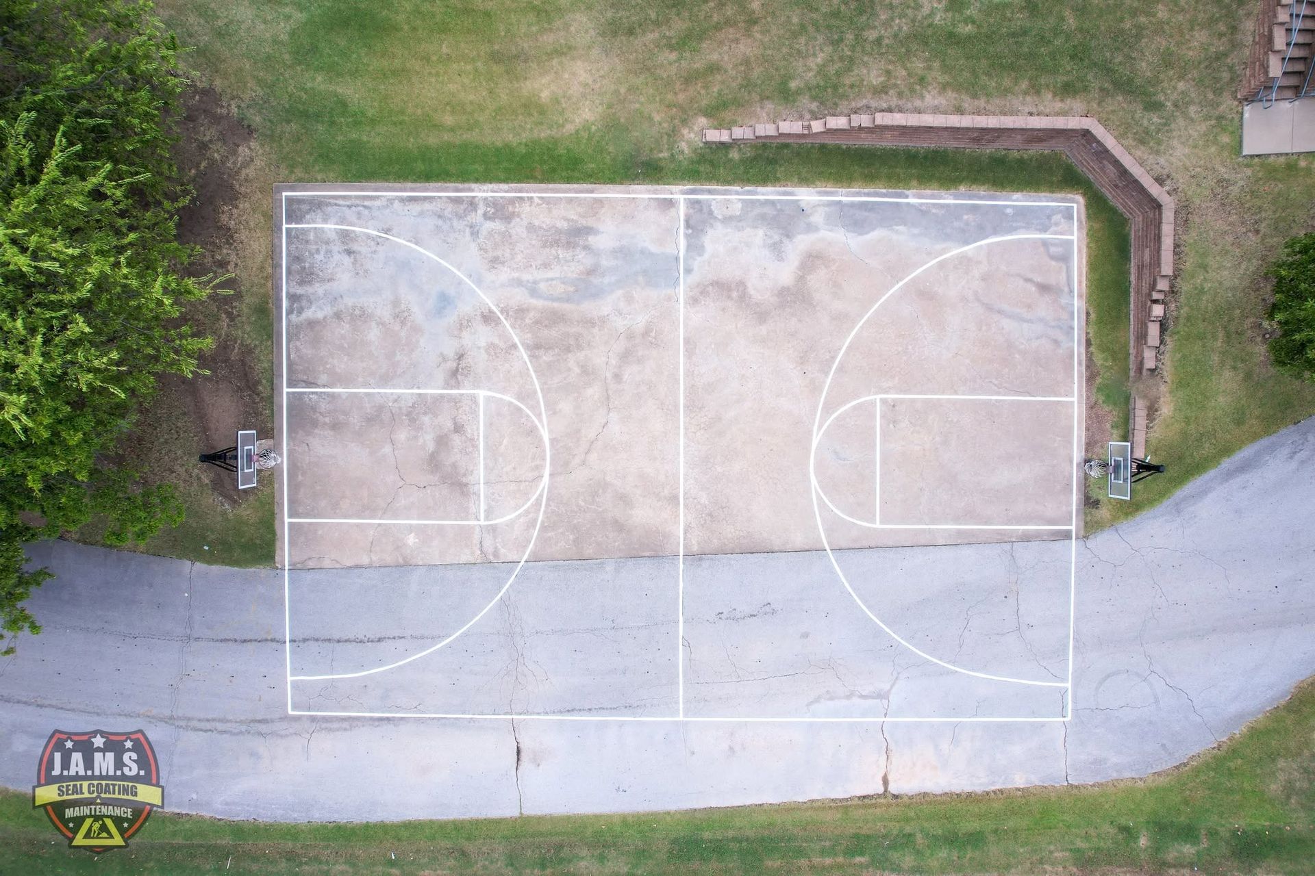 Overhead view of an empty outdoor basketball court beside a driveway and grassy area.