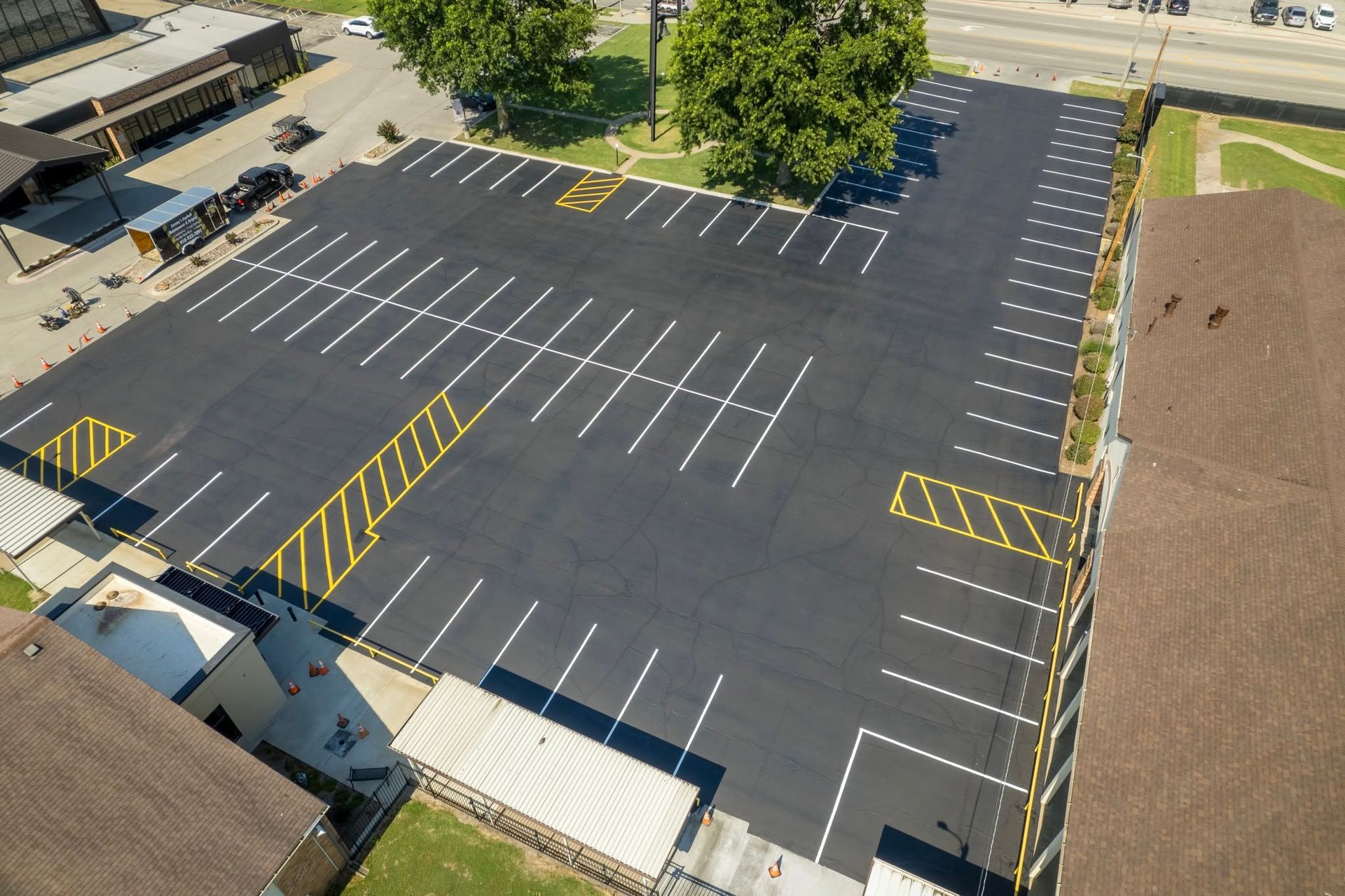 Empty paved parking lot with white and yellow parking lines beside a building and trees