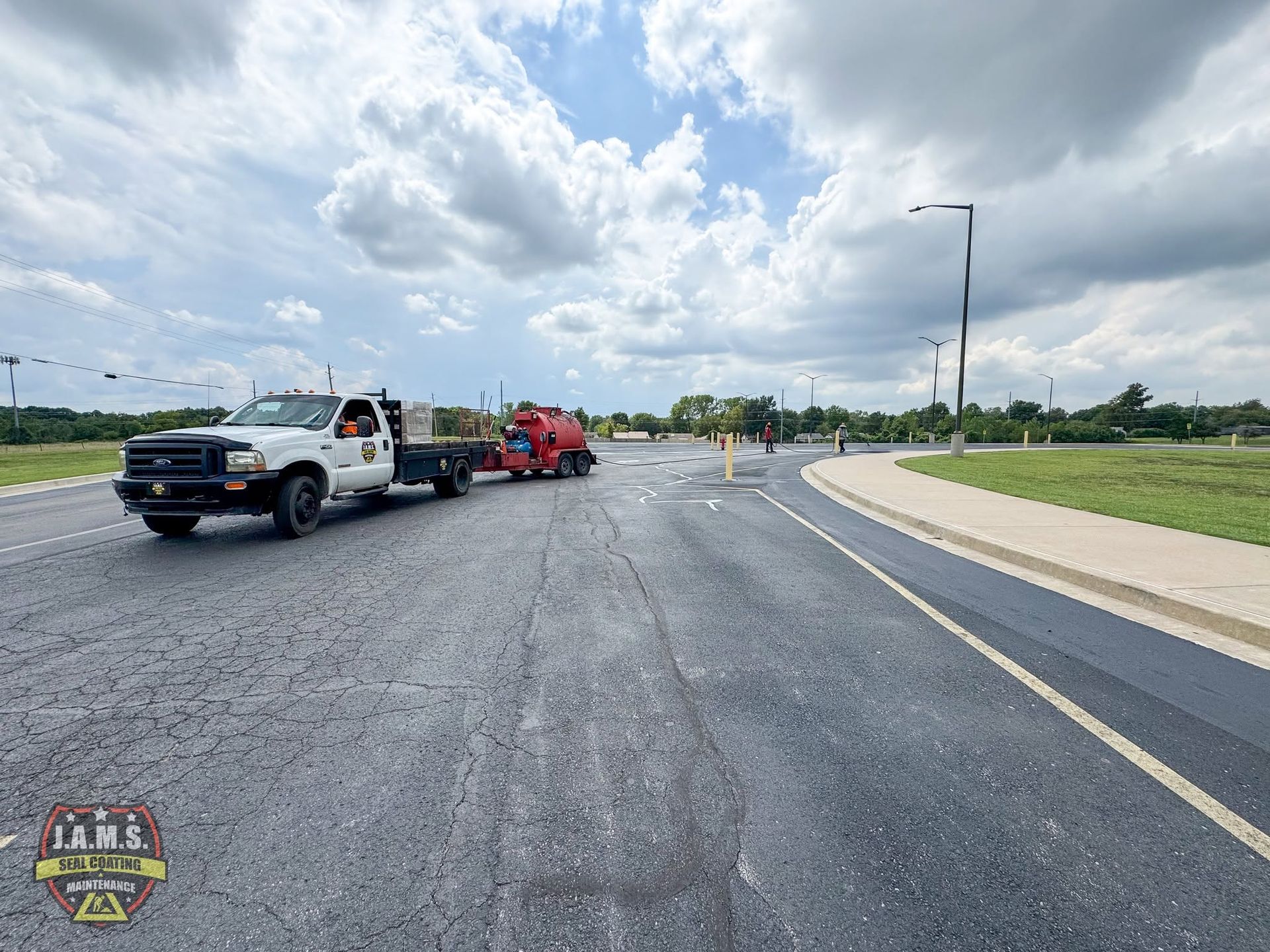 Tow truck towing red car on a rural road under cloudy sky; workers nearby and lane cones visible