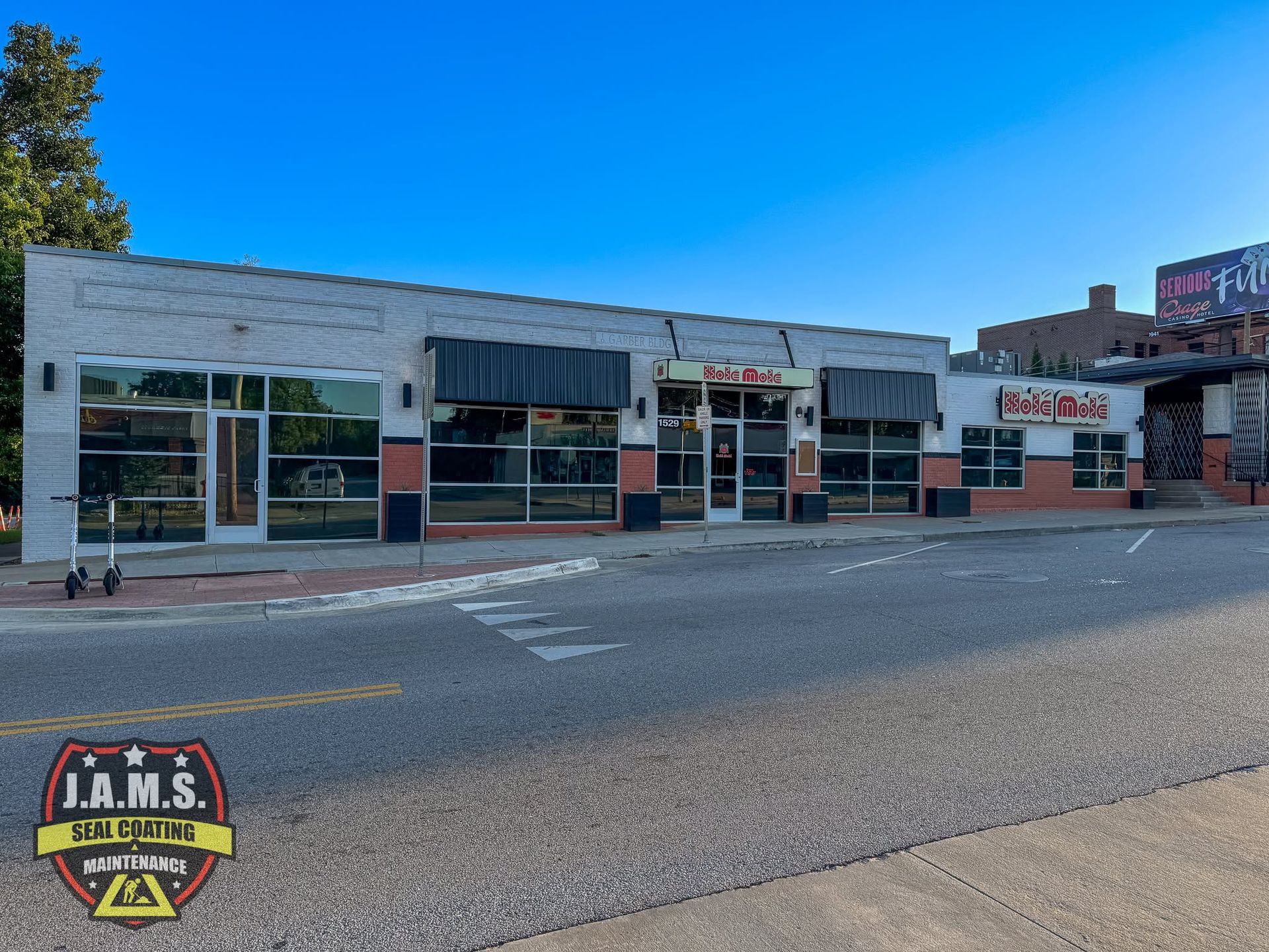 Street view of a small row of storefronts with large windows and signs under a clear blue sky.