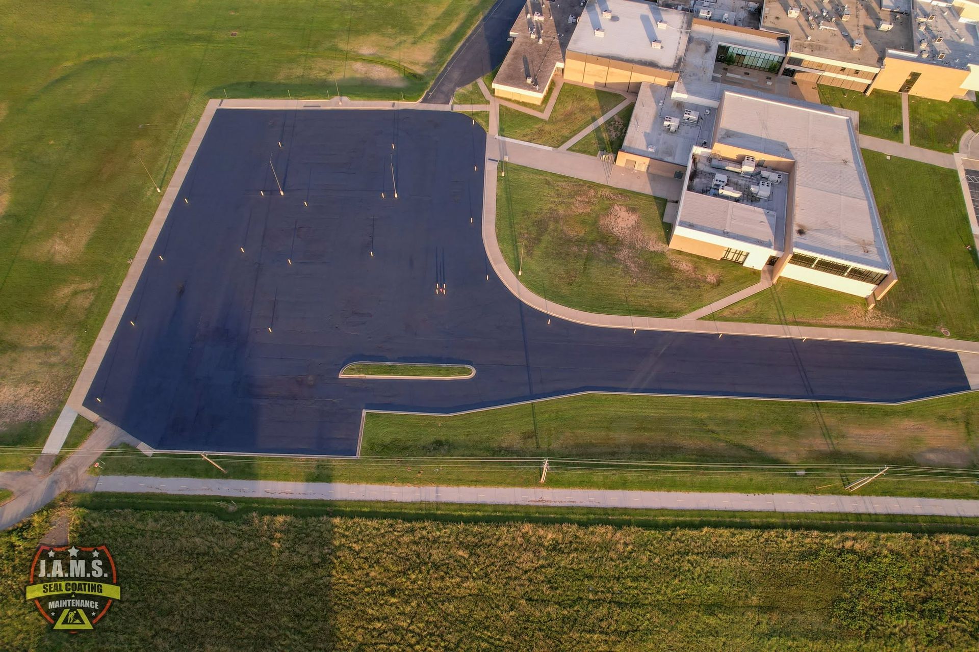 Aerial view of a paved parking lot beside buildings and grass fields at dusk.
