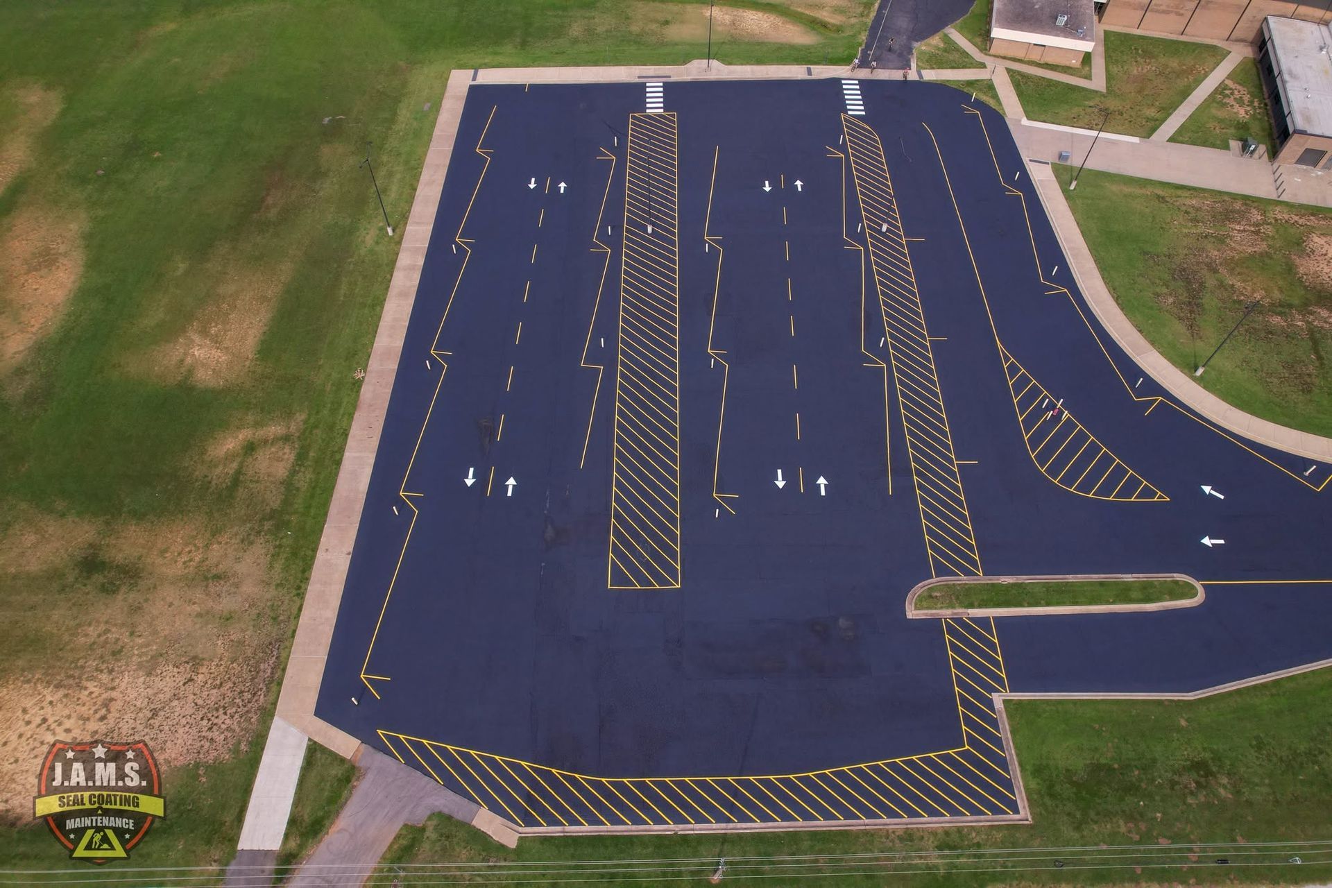 Aerial view of a dark blue paved lot with white and yellow lane markings and grassy borders