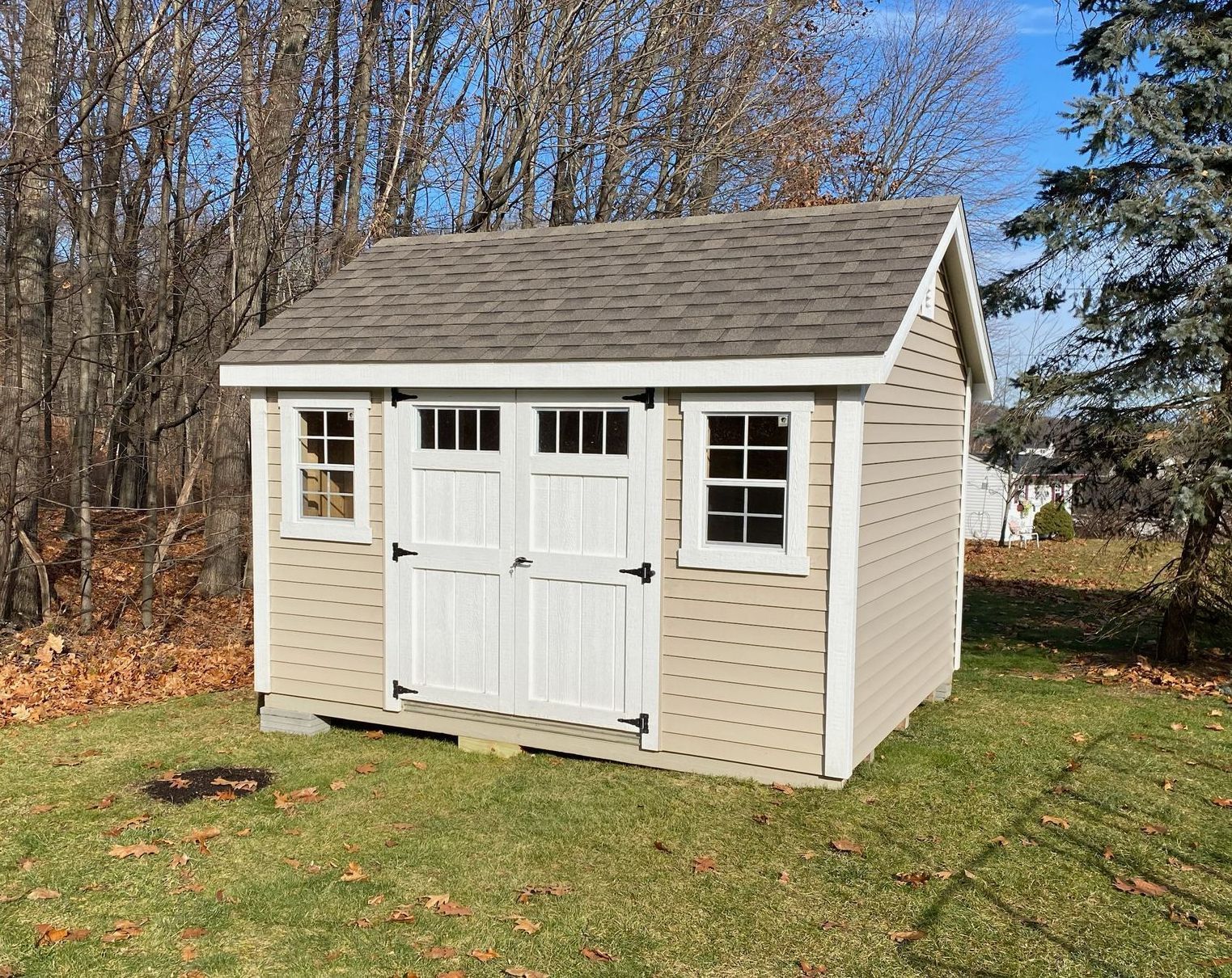 Tan shed with white trim, double doors, and two windows, set on green grass.