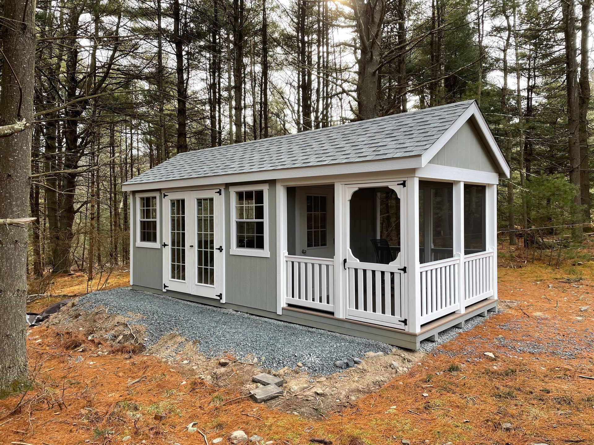 Gray and white cabin with a screened porch in a wooded area.