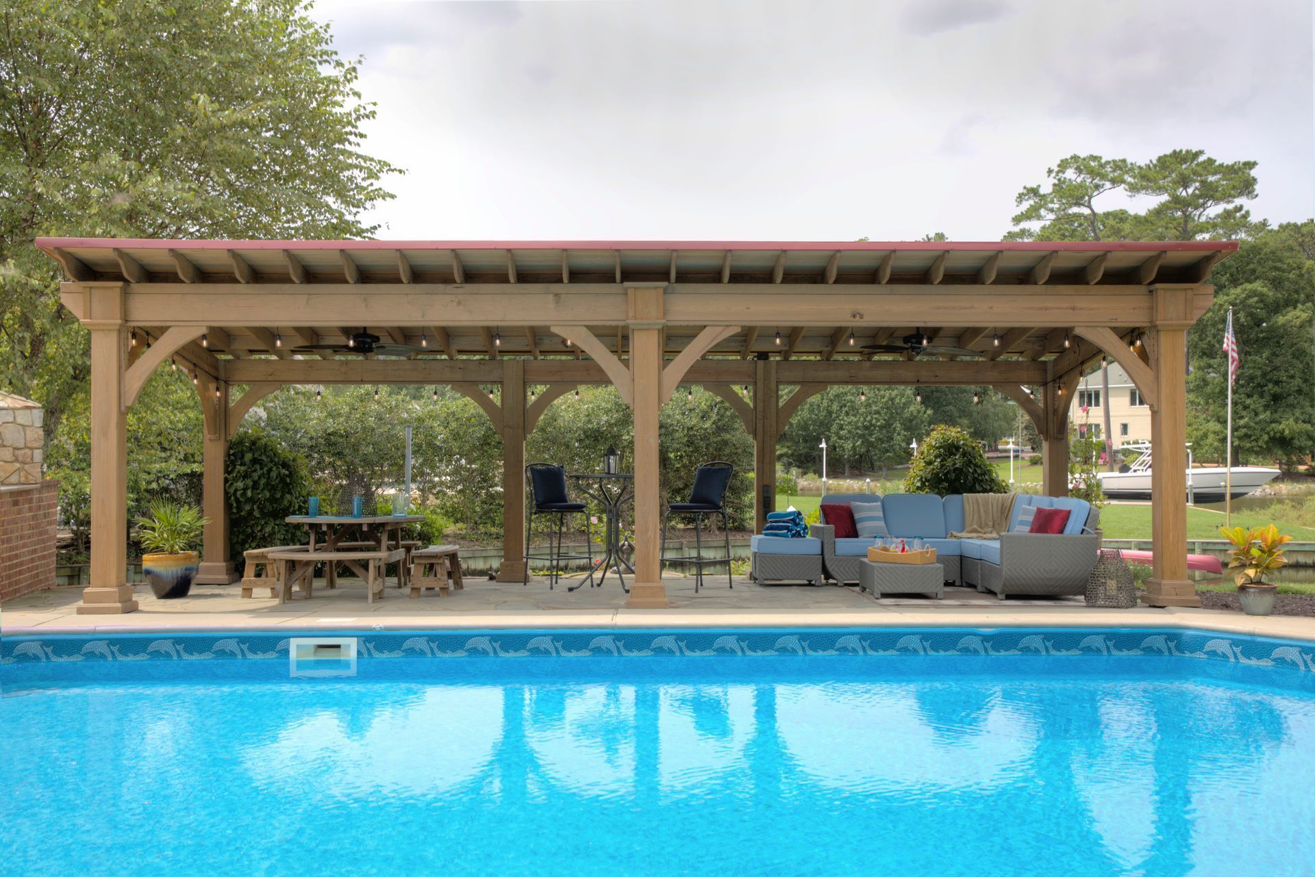 Poolside pergola with seating and table, overlooking a blue-tiled pool.
