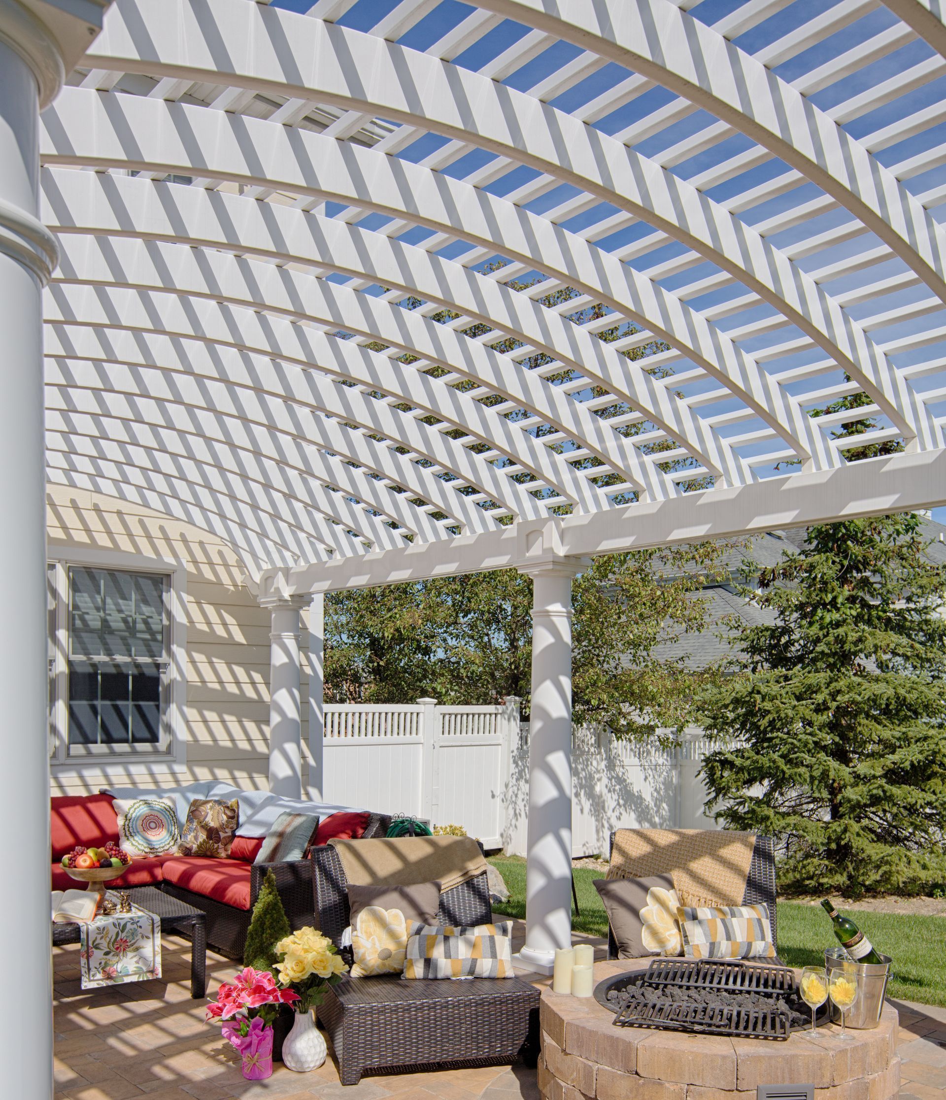 White pergola over outdoor seating area with colorful cushions and flowers.