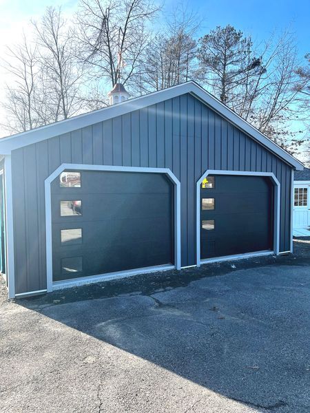 Two-bay garage with dark gray doors, blue siding, and small windows. Sunny day, clear sky.