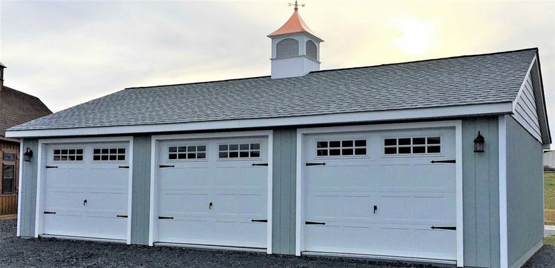 Three-bay garage with a cupola. The building is light blue with white doors, and grey roofing.