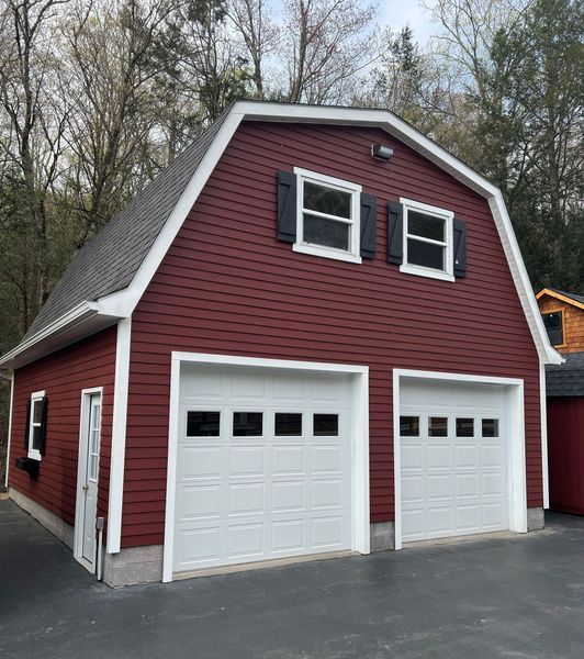 Two-story red barn with two white garage doors, two windows, and black shutters.