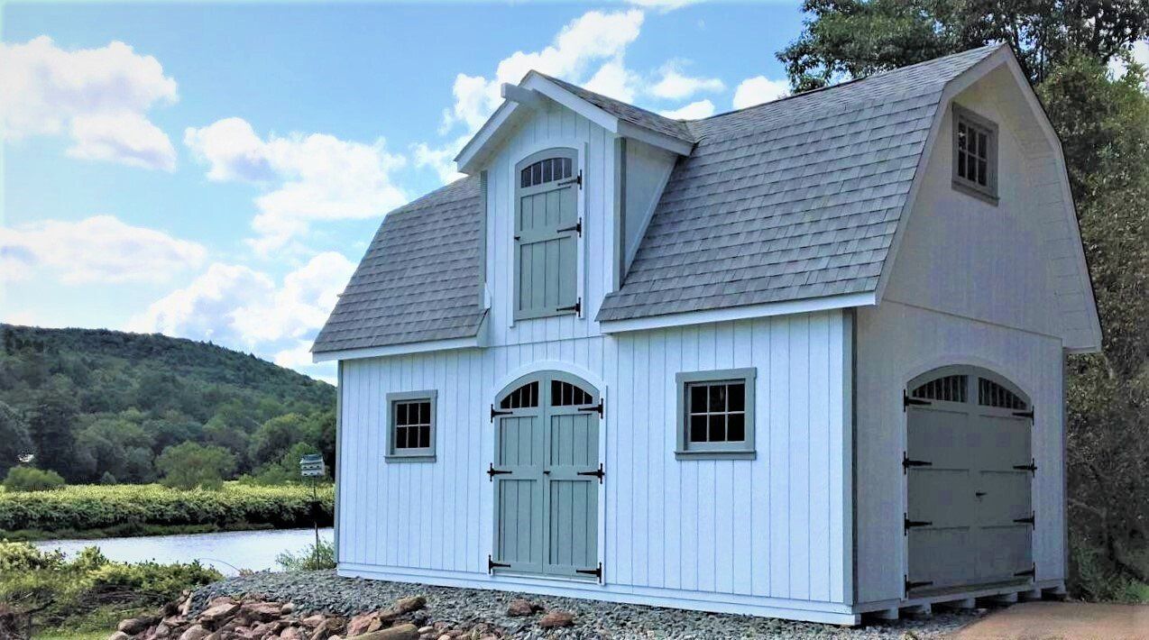 White barn-style shed with gray roof and light green doors/trim, near a river, under a partly cloudy sky.