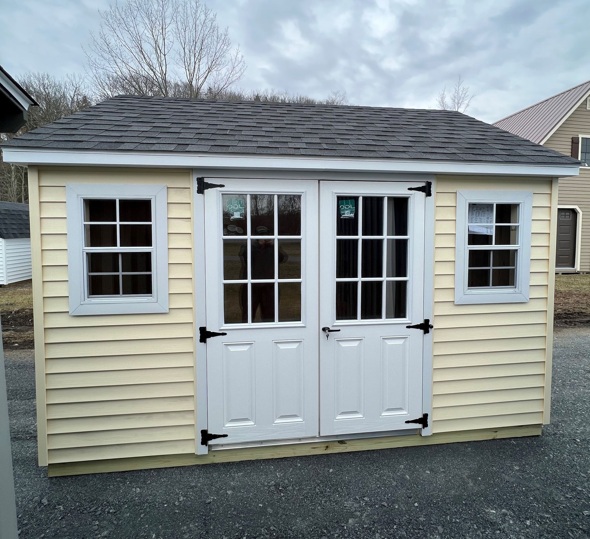 Yellow shed with double doors and windows, black hinges, on a cloudy day.