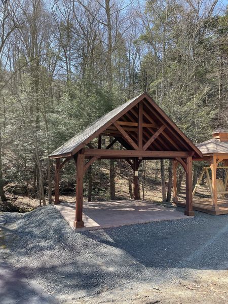 Wooden pavilion with a brick patio in a wooded area.