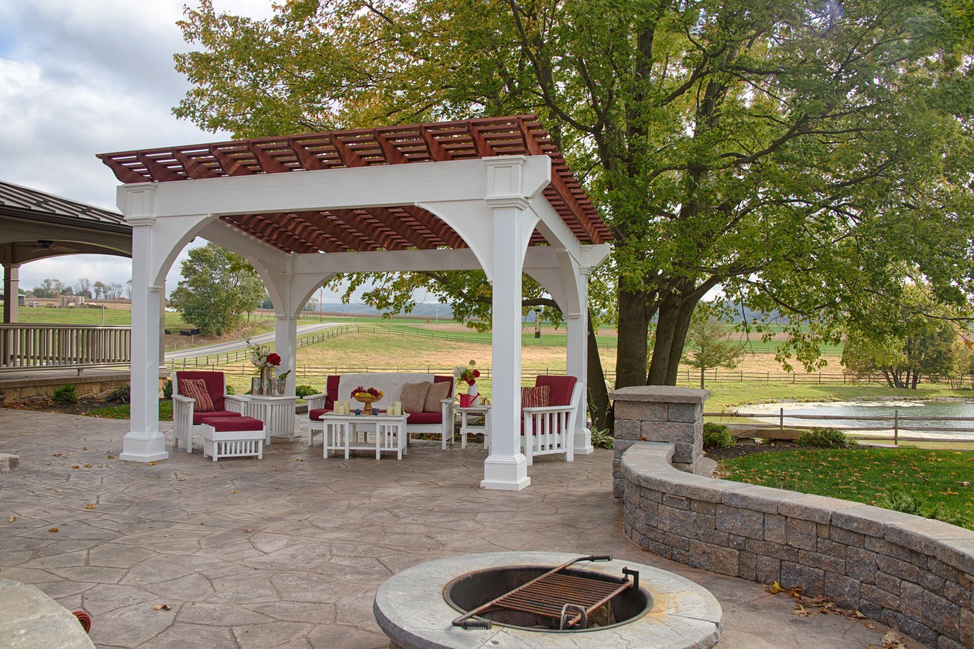 White pergola with red accents over patio furniture, overlooking a field.