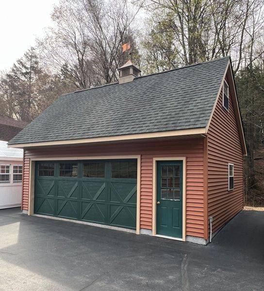 Two-story detached garage with green door and garage door, brown siding, and a green roof.