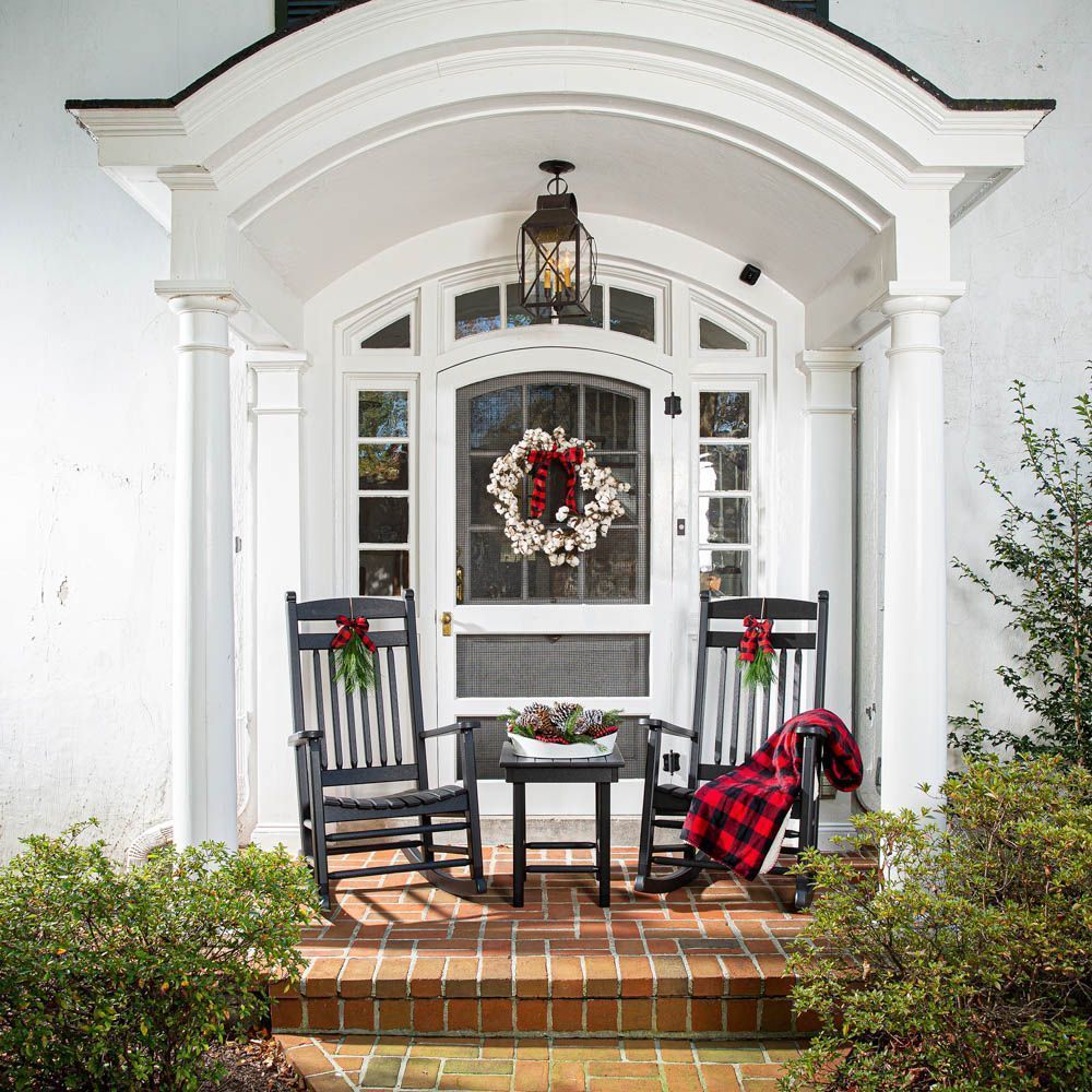 Front porch decorated for Christmas with rocking chairs, wreath, and red plaid blanket.