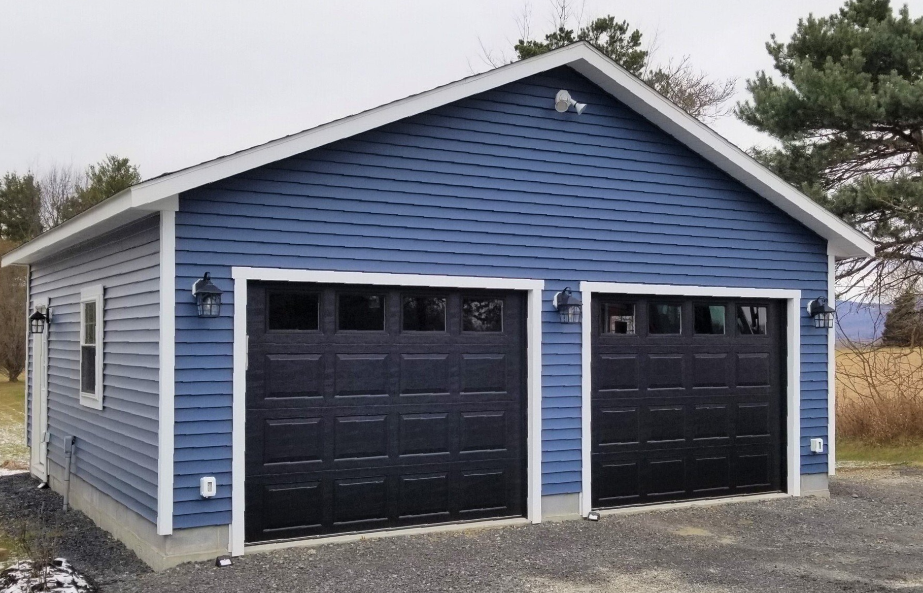 Two-car blue garage with black doors, white trim, and outdoor lights.