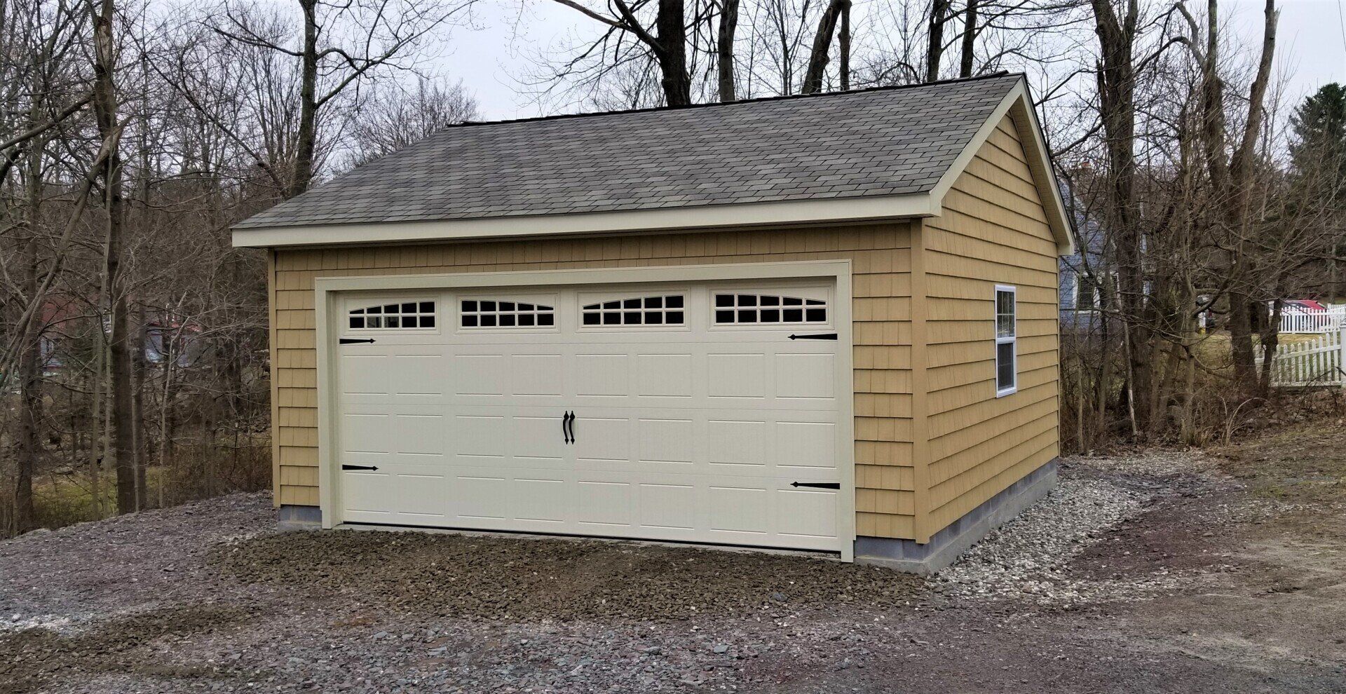 Tan garage with a white door and a gray roof, set on gravel.