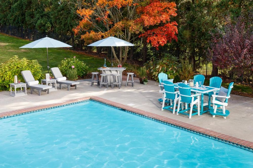 Poolside patio with turquoise furniture, umbrellas, and a bar, surrounded by fall foliage.