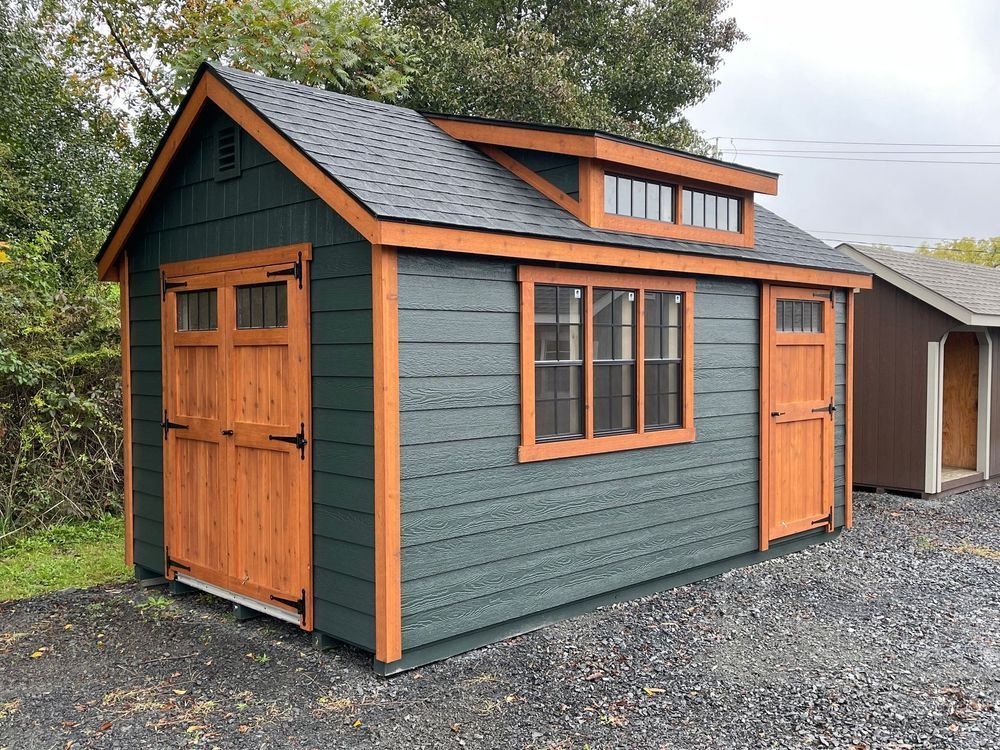 Green shed with orange trim and doors, small window, and a dormer.