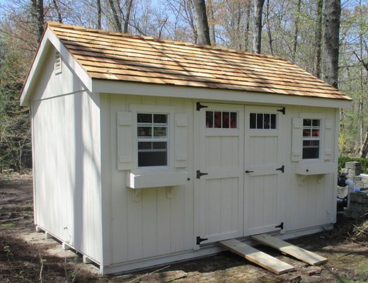Tan shed with brown roof, three doors, two windows with shutters, and two wooden ramps.