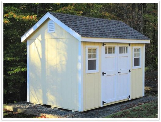 Yellow shed with white trim, double doors, and two windows against a wooded backdrop.