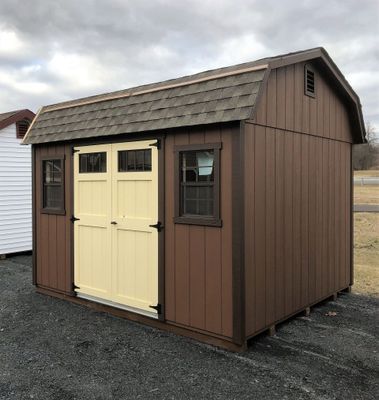Brown shed with cream doors and dark trim against a cloudy sky.
