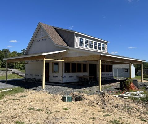 Building under construction; two-story structure with a large covered porch, on a sunny day.